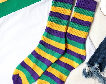 May include: A pair of striped socks in purple, green, and yellow. The socks are folded and laid out on a white surface.