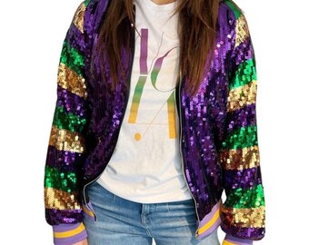 May include: A sequined bomber jacket in purple, green, and gold stripes. The jacket has a zipper closure and ribbed cuffs with yellow and purple stripes. A white t-shirt with the text "LA" is visible underneath the jacket.
