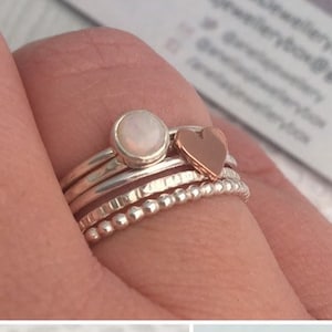 May include: Set of three silver stacking rings with a white opal gemstone on the top ring. The rings are textured and have a beaded design.