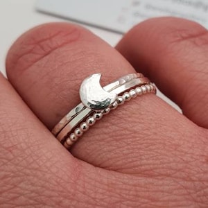 May include: A set of three silver rings, one with a hammered crescent moon design, and two with textured bands.