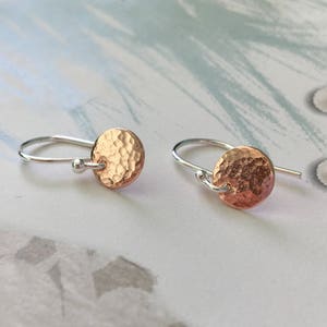 以下が含まれることがあります： ハンマード銅のディスクが付いたシルバーフープイヤリングのペア。イヤリングはシンプルでエレガントで、あらゆる機会に最適なギフトになります。