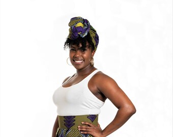 May include: A woman with curly hair is wearing a white tank top, a green and purple patterned skirt, and a green and purple patterned head wrap. She is smiling and looking at the camera.