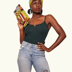 Può includere: Una donna indossa una canotta verde, jeans blu con toppe floreali e un turbante colorato. Tiene in mano una pochette colorata.