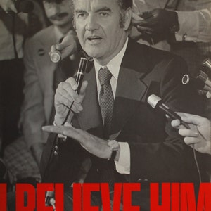 Puede incluir: Una fotografía en blanco y negro de un hombre hablando en un micrófono. Lleva traje y corbata. El texto "I BELIEVE HIM" está impreso en letras rojas en la parte inferior de la imagen.