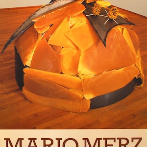 May include: A sculpture made of yellow wax, with a black metal base and a mounted animal head with horns. The sculpture is titled "Dal Miele Alle Ceneri 1984" and is by artist Mario Merz. The text "SPERONE WESTWATER 16 NOV-21 DEC/LEO CASTELLI 23 NOV-21 DEC 142 GREENE STREET NEW YORK" is printed below the sculpture.