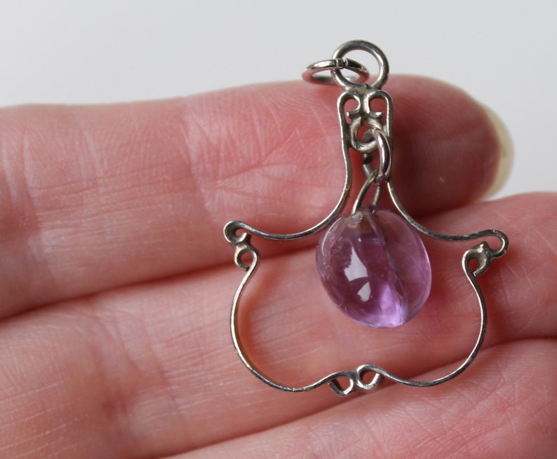 May include: A silver charm with a delicate, openwork design in the shape of a hand holding a round, purple amethyst stone.