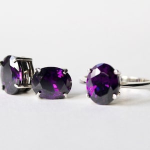 May include: A set of three silver rings with large, oval-shaped, purple gemstones. The rings are on a white surface.