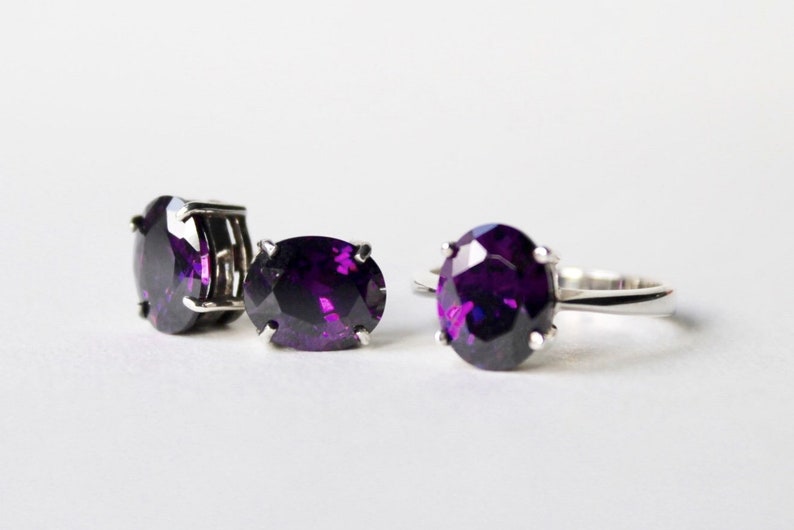 May include: A set of three silver rings with large, oval-shaped, purple gemstones. The rings are on a white surface.