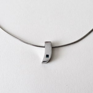 Peut inclure: Un collier en chaîne argent avec un petit pendentif argenté orné d'une seule pierre précieuse bleue.