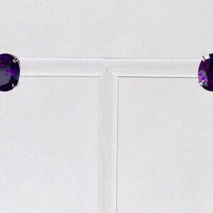 May include: A pair of silver stud earrings with oval-shaped purple gemstones.