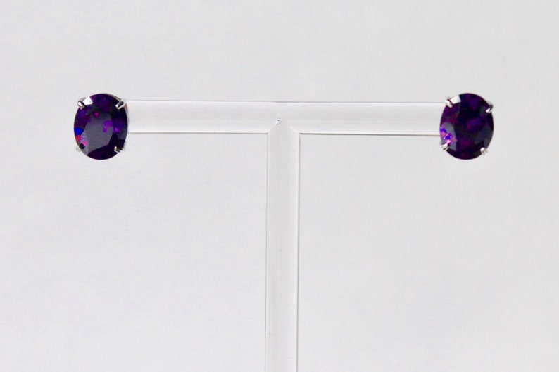 May include: A pair of silver stud earrings with oval-shaped purple gemstones.