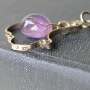May include: A silver charm with a purple amethyst stone and the inscription "925" on the back.