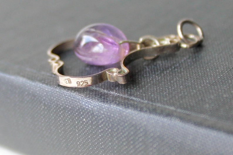 May include: A silver charm with a purple amethyst stone and the inscription "925" on the back.