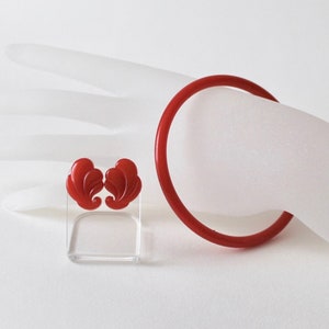 May include: A set of red plastic earrings and a red plastic bangle bracelet. The earrings are shaped like stylised feathers.