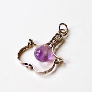 May include: A silver charm in the shape of a bird with a purple amethyst gemstone hanging from it.