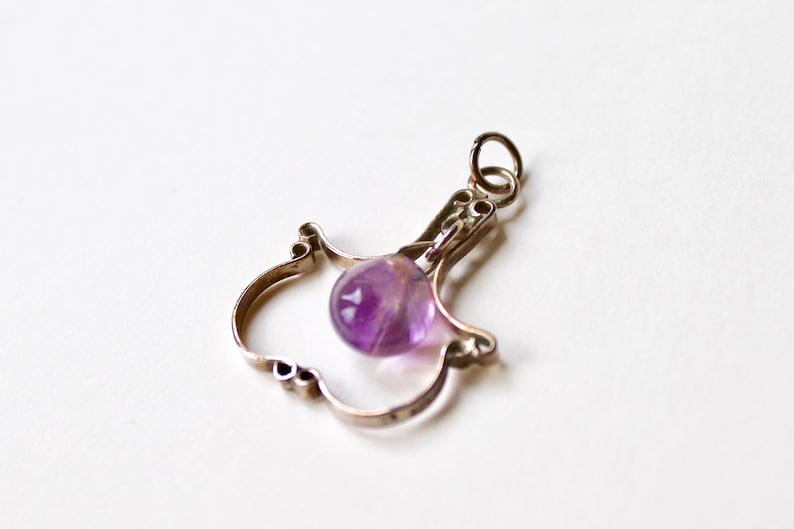 May include: A silver charm in the shape of a bird with a purple amethyst gemstone hanging from it.