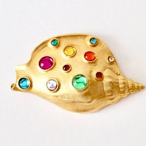 Op de afbeelding: Een gouden schelp broche met verschillende gekleurde strass steentjes. De broche is gevormd als een schelp met een spiraalvormig ontwerp.