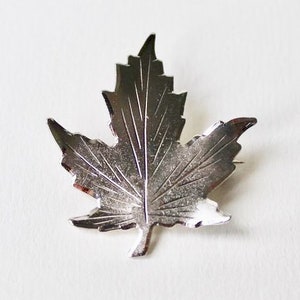 Op de afbeelding: Een zilveren esdoornblad broche met een gedetailleerd ontwerp.