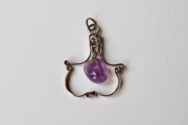 May include: A silver pendant with a delicate, openwork design, featuring a purple amethyst gemstone.