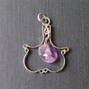 May include: A silver pendant with a delicate, ornate design features a dangling amethyst gemstone. The pendant is shaped like a teardrop and has a loop at the top for attaching to a chain.