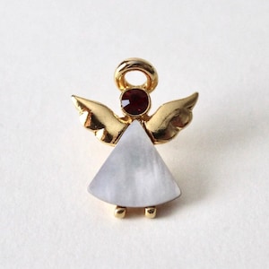 Peut inclure: Une broche d'ange en or avec une robe blanche irisée et un strass rouge au centre.