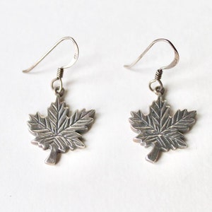 May include: A pair of silver maple leaf earrings with a simple hook design.