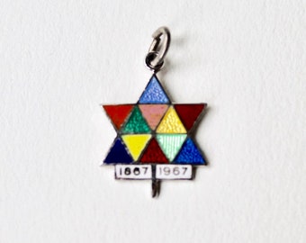 May include: Silver charm with a colorful enamel star of David design. The star is made up of six triangles, each a different color: red, pink, green, yellow, blue, and dark blue. The charm also has a silver bar with the dates "1867 1967" on it.