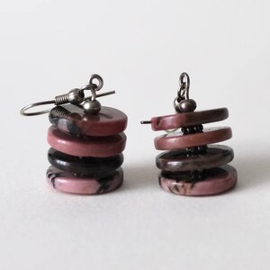 Op de afbeelding: Een paar oorbellen met een gestapelde vorm. Elke oorbel heeft vier ronde, roze en zwarte stenen kralen met een zilveren haak.