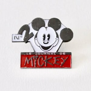 May include: A black and white Mickey Mouse pin with the text "Le Journal de Mickey" in red and white. The pin is numbered "N° 20".