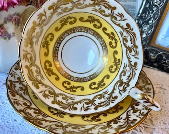 May include: A vintage teacup and saucer set. The teacup and saucer are yellow and white with gold filigree detailing. The teacup has a handle and a scalloped rim. The saucer is round and has a matching design. The set is likely made of porcelain.