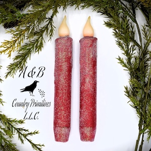 May include: Two red glitter pillar candles with a white wax flame tip. The candles are approximately 18 cm tall.