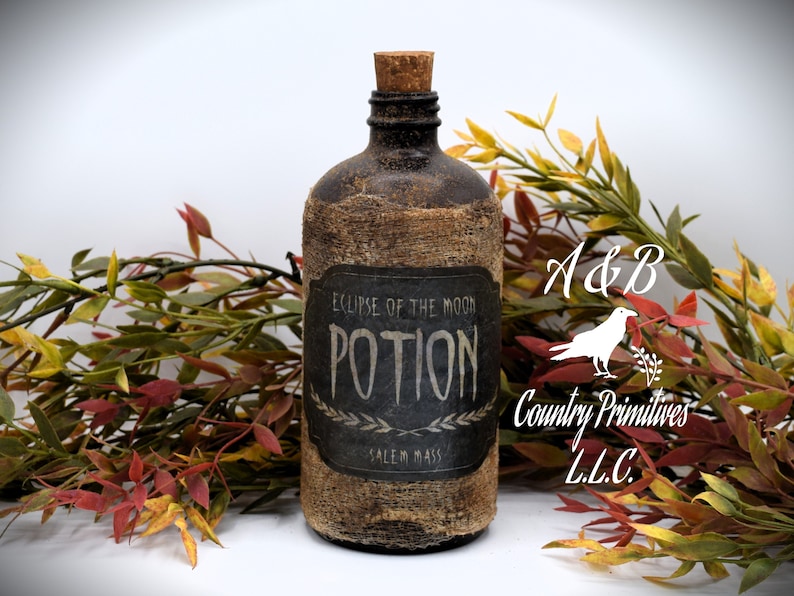An antique brown bottle labeled "Eclipse of the Moon Potion, Salem Mass" is in front of autumn-colored foliage. The bottle has a cork stopper and rustic appearance.