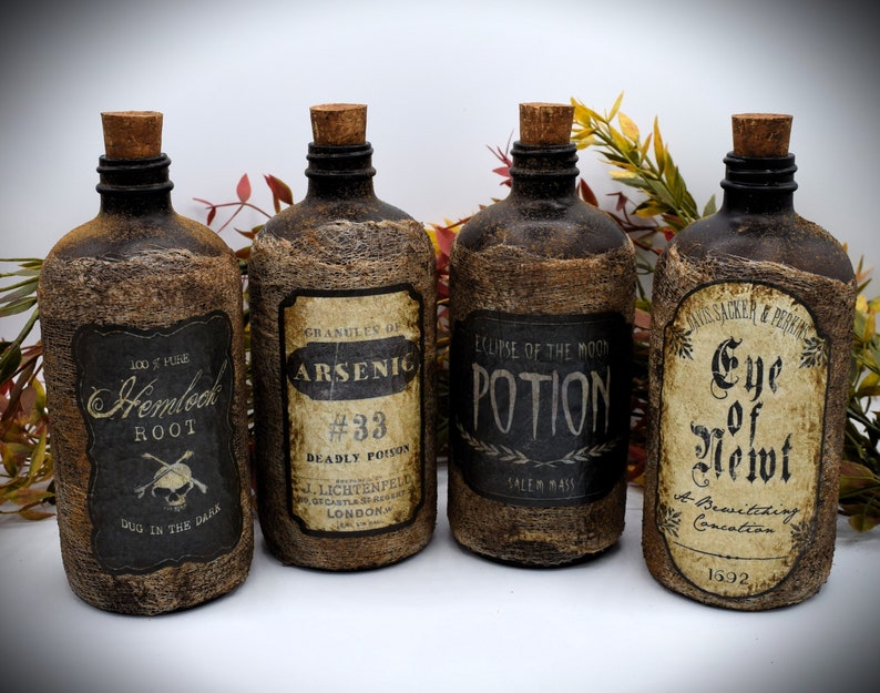 Four rustic bottles with cork stoppers and vintage-style labels. The labels read: "Hemlock Root," "Arsenic #33," "Eclipse of the Moon Potion," and "Eye of Newt." The bottles are surrounded by autumn leaves.