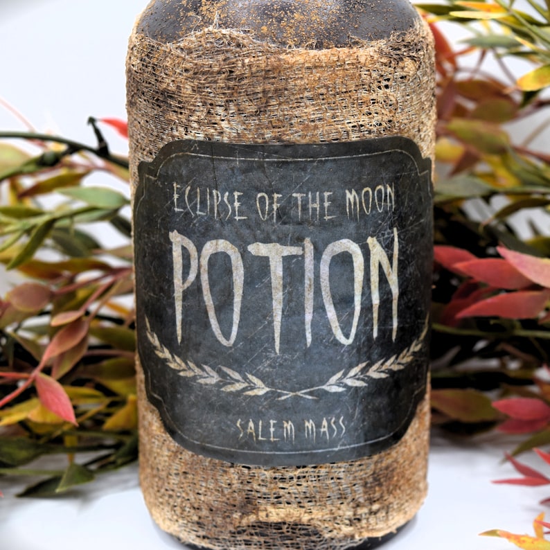 An antique brown bottle labeled "Eclipse of the Moon Potion, Salem Mass" is in front of autumn-colored foliage. The bottle has a rustic appearance.
