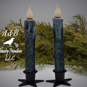 May include: Two black and green glitter candles with white frosted tips and a white flame on each. The candles are on black star-shaped candle holders. A&B Country Primitives L.L.C. is printed on the image.
