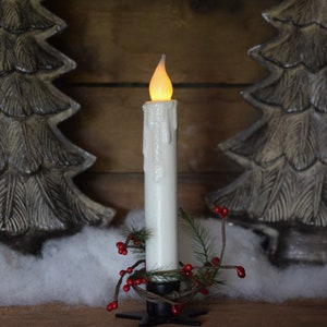 7 inch, white taper candle coated in shimmering glitter, with wax dipped, flame shaped candle bulb  glowing yellow/ orange, displayed in black wrought iron, star shaped holder, with decorative pine candle ring.  Fake snow and Christmas decor behind.