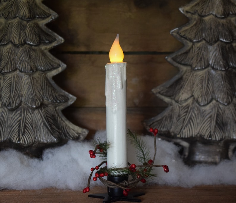 7 inch, white taper candle coated in shimmering glitter, with wax dipped, flame shaped candle bulb  glowing yellow/ orange, displayed in black wrought iron, star shaped holder, with decorative pine candle ring.  Fake snow and Christmas decor behind.