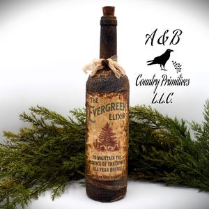 May include: A rustic brown glass bottle with a cork stopper and a label that reads "The Evergreen Elixir" with a small evergreen tree illustration. The label also says "To maintain the essence of Christmas all year round".