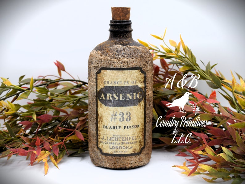 An antique brown bottle labeled "Granules of Arsenic #33 Deadly Poison" is in front of autumn-colored foliage. The bottle has a cork stopper and rustic appearance.