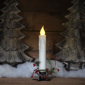 7 inch, white taper candle coated in shimmering glitter, with wax dipped, flame shaped candle bulb  glowing yellow/ orange, displayed in black wrought iron, star shaped holder, with decorative pine candle ring.  Fake snow and Christmas decor behind.