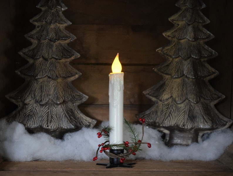 7 inch, white taper candle coated in shimmering glitter, with wax dipped, flame shaped candle bulb  glowing yellow/ orange, displayed in black wrought iron, star shaped holder, with decorative pine candle ring.  Fake snow and Christmas decor behind.
