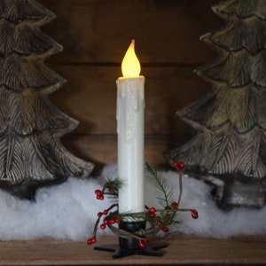 7 inch, white taper candle coated in shimmering glitter, with wax dipped, flame shaped candle bulb  glowing yellow/ orange, displayed in black wrought iron, star shaped holder, with decorative pine candle ring.  Fake snow and Christmas decor behind.