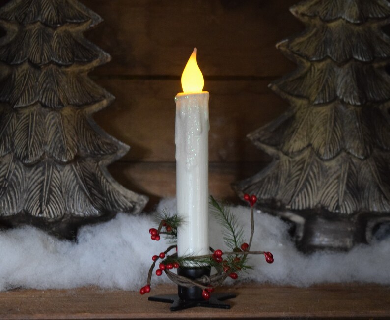 7 inch, white taper candle coated in shimmering glitter, with wax dipped, flame shaped candle bulb  glowing yellow/ orange, displayed in black wrought iron, star shaped holder, with decorative pine candle ring.  Fake snow and Christmas decor behind.