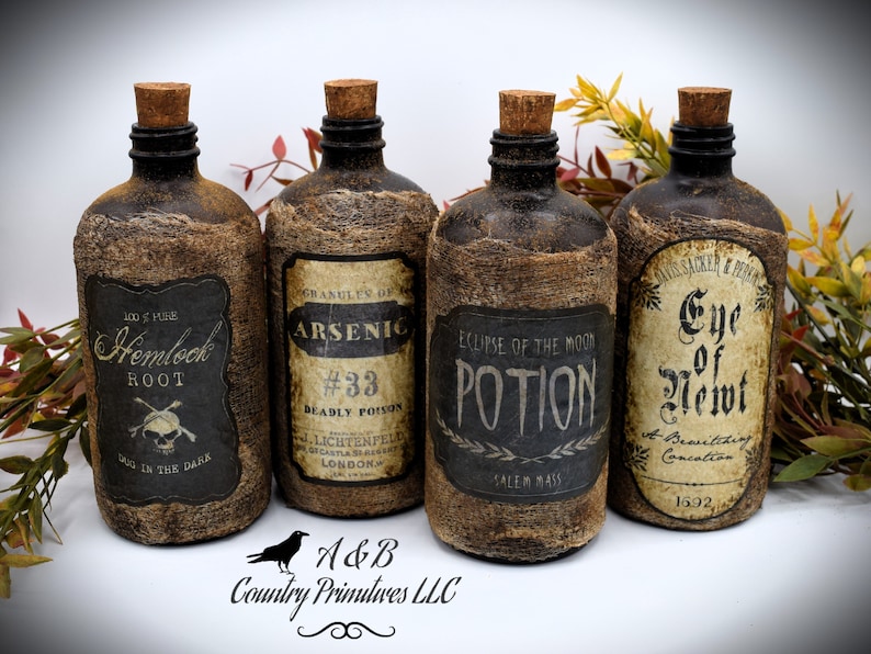 Four rustic glass bottles with cork stoppers and vintage-style labels. The labels read: Hemlock Root, ,Arsenic #33, Eclipse of the Moon Potion, and Eye of Newt. The bottles are surrounded by autumn leaves.