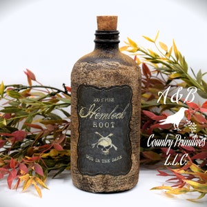 An antique brown bottle labeled "100% Pure Hemlock Root Dug in the Dark" with a skull and crossbones symbol is in front of autumn-colored foliage. The bottle has a cork stopper and rustic appearance.