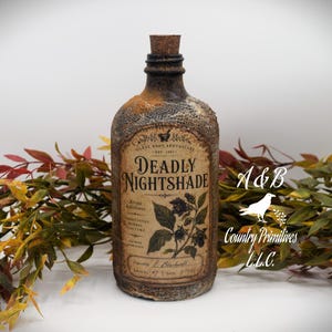 May include: A glass bottle with a cork stopper, featuring a textured, weathered finish and a label that reads Deadly Nightshade, Milky Root Apothecary, Est 1897, Traditional Herbal Tincture, and E. Blackwell. The bottle is surrounded by autumn foliage.