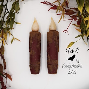 May include: Two brown battery-operated candles with a warm white LED light. The candles have a rustic, distressed look and are perfect for adding a touch of ambience to any space.