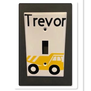 May include: White light switch cover with a yellow dump truck graphic and the name "Trevor" in black lettering.