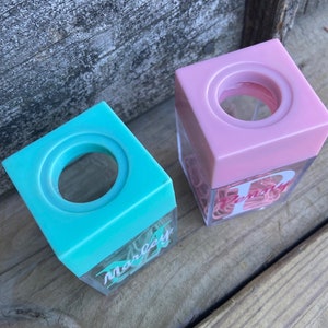 K&ouml;nnte beinhalten: Zwei quadratische, durchsichtige Plastikbeh&auml;lter mit rosa und blauen Deckeln. Die Beh&auml;lter sind mit rosa B&uuml;roklammern gef&uuml;llt und haben einen wei&szlig;en Buchstaben an der Seite. Der rosa Beh&auml;lter hat den Buchstaben "P" und der blaue Beh&auml;lter den Namen "Marley" an der Seite.