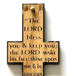 May include: A wooden cross with a black border and a burnt wood finish. The cross features a bible verse from Numbers 6:24-26, "The Lord bless you and keep you; the Lord make his face shine upon you and be gracious to you; the Lord turn his face toward you and give you peace."